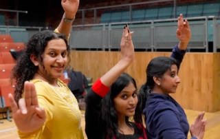 Three performers with arms raised like trees